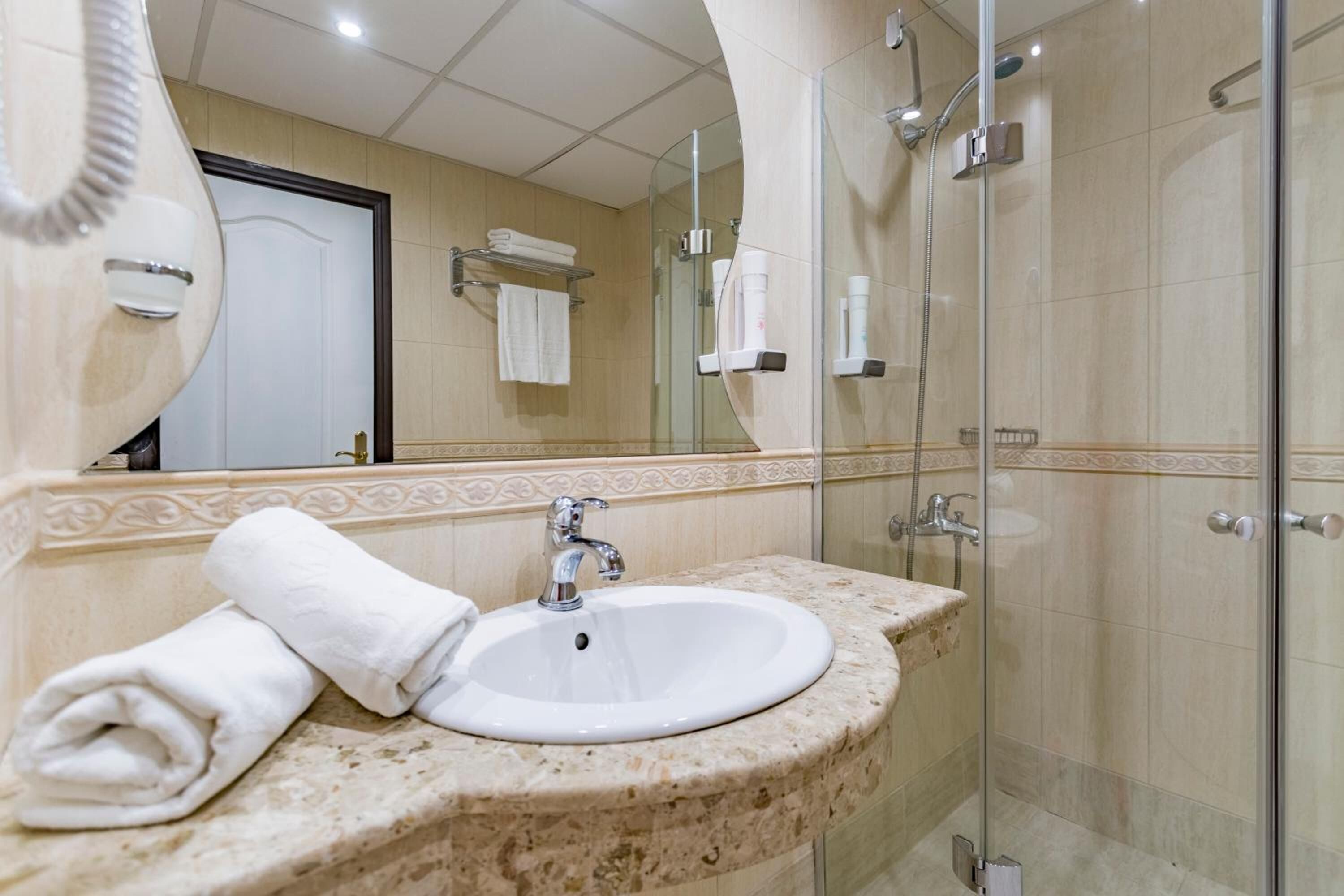 A bathroom with a marble sink, a glass shower enclosure, and a mirror reflecting a towel rack and door.