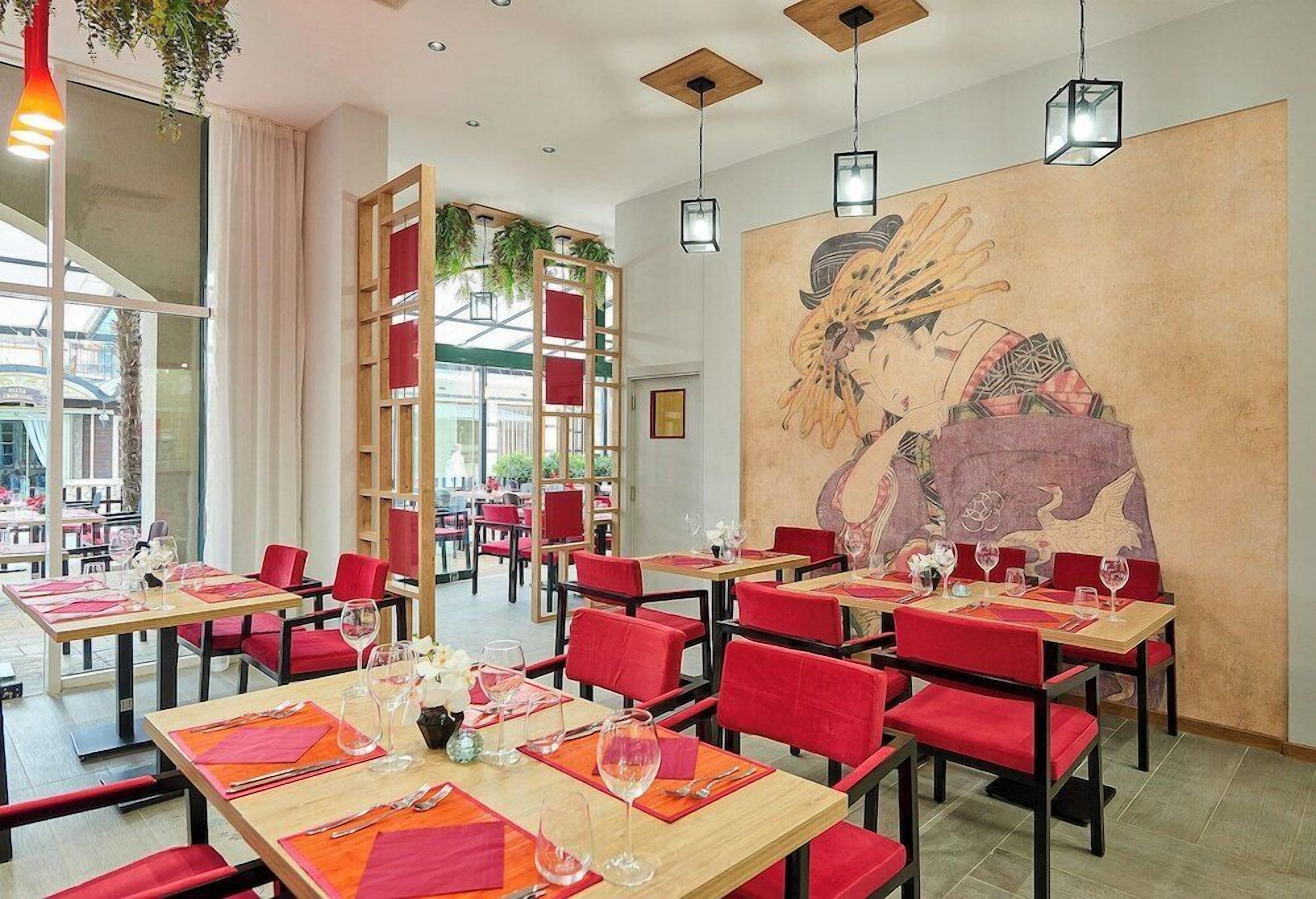 A restaurant with red chairs and tables, a large mural on the wall, and hanging plants.