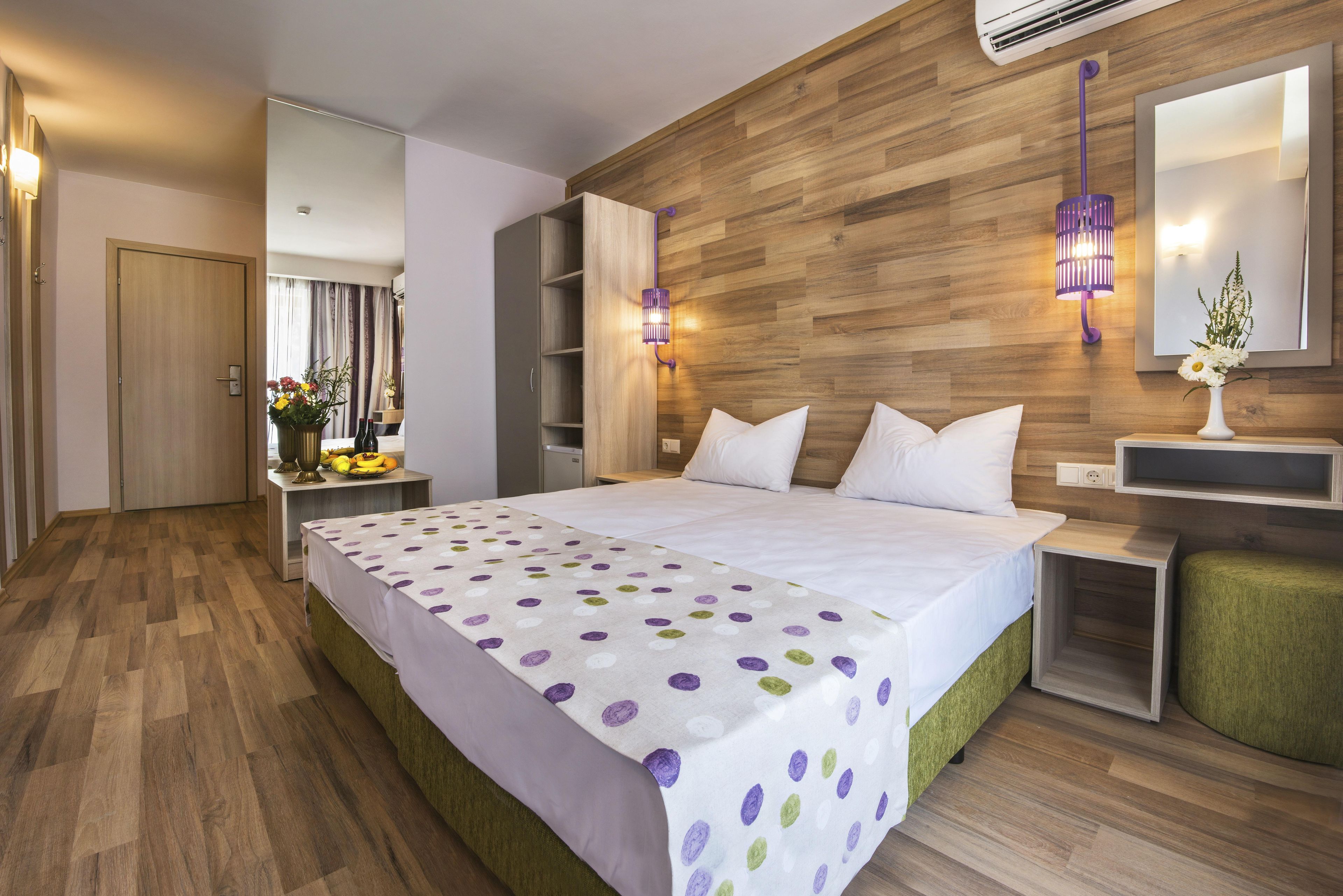A modern bedroom with a wooden wall, a bed with white bedding, a nightstand, and a wall-mounted lamp.