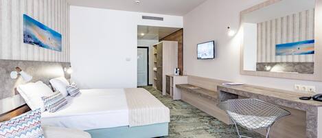 A hotel room with a bed, a desk, a chair, a TV, and artwork on the walls.