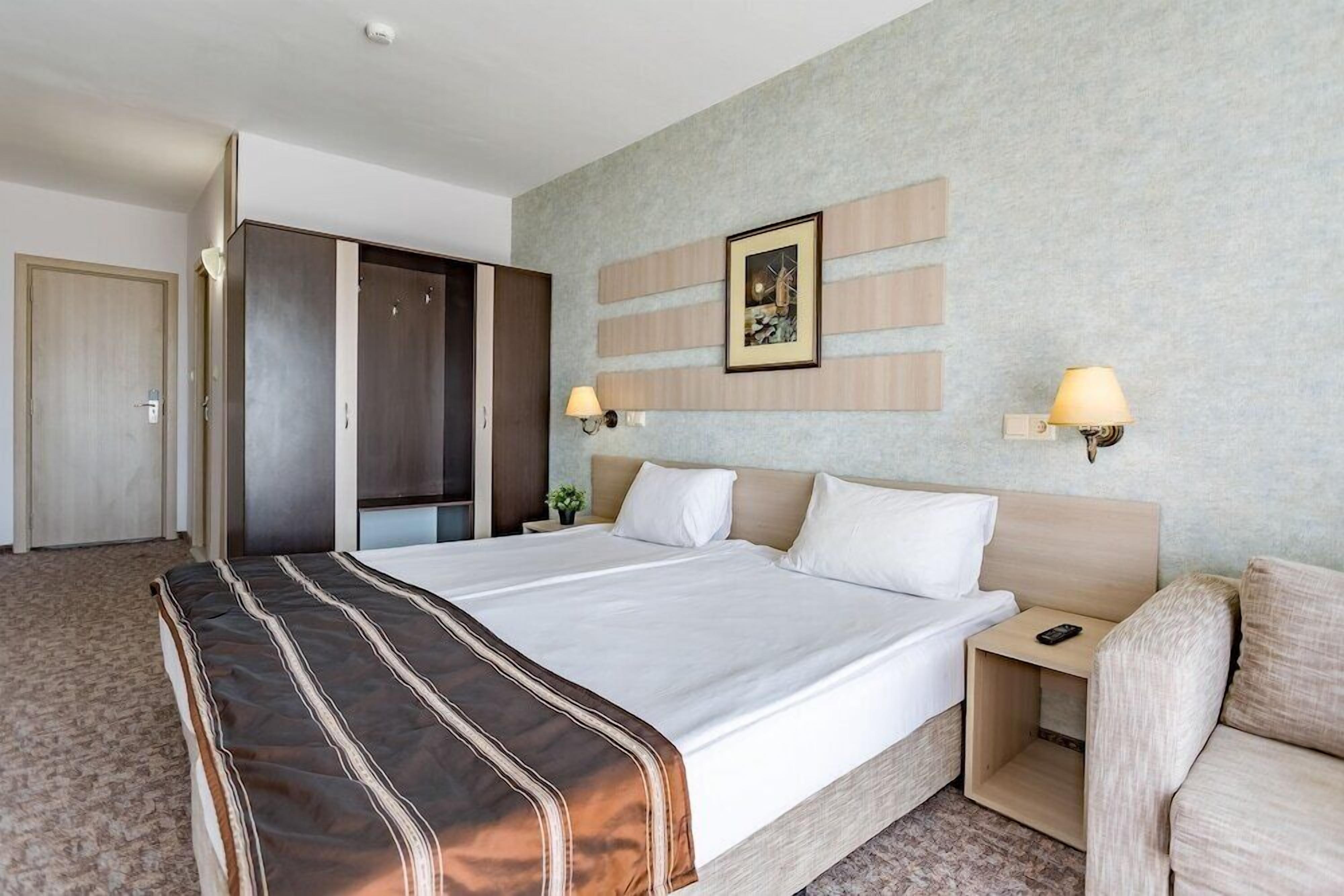 Una camera d'albergo con un letto grande, un comodino, una sedia, un armadio e un quadro appeso al muro.
