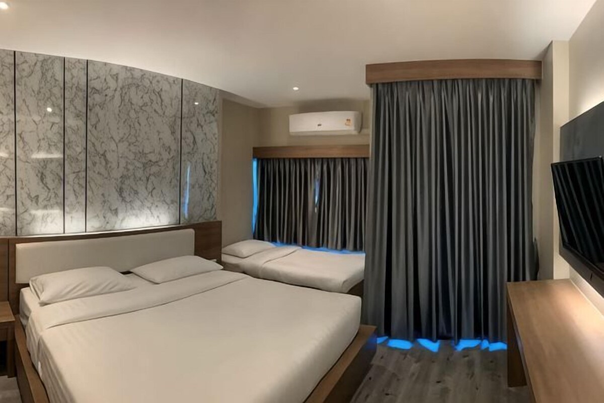 Ein Hotelzimmer mit zwei Betten, einer Marmorwand, einem Fernseher und einem Vorhang.