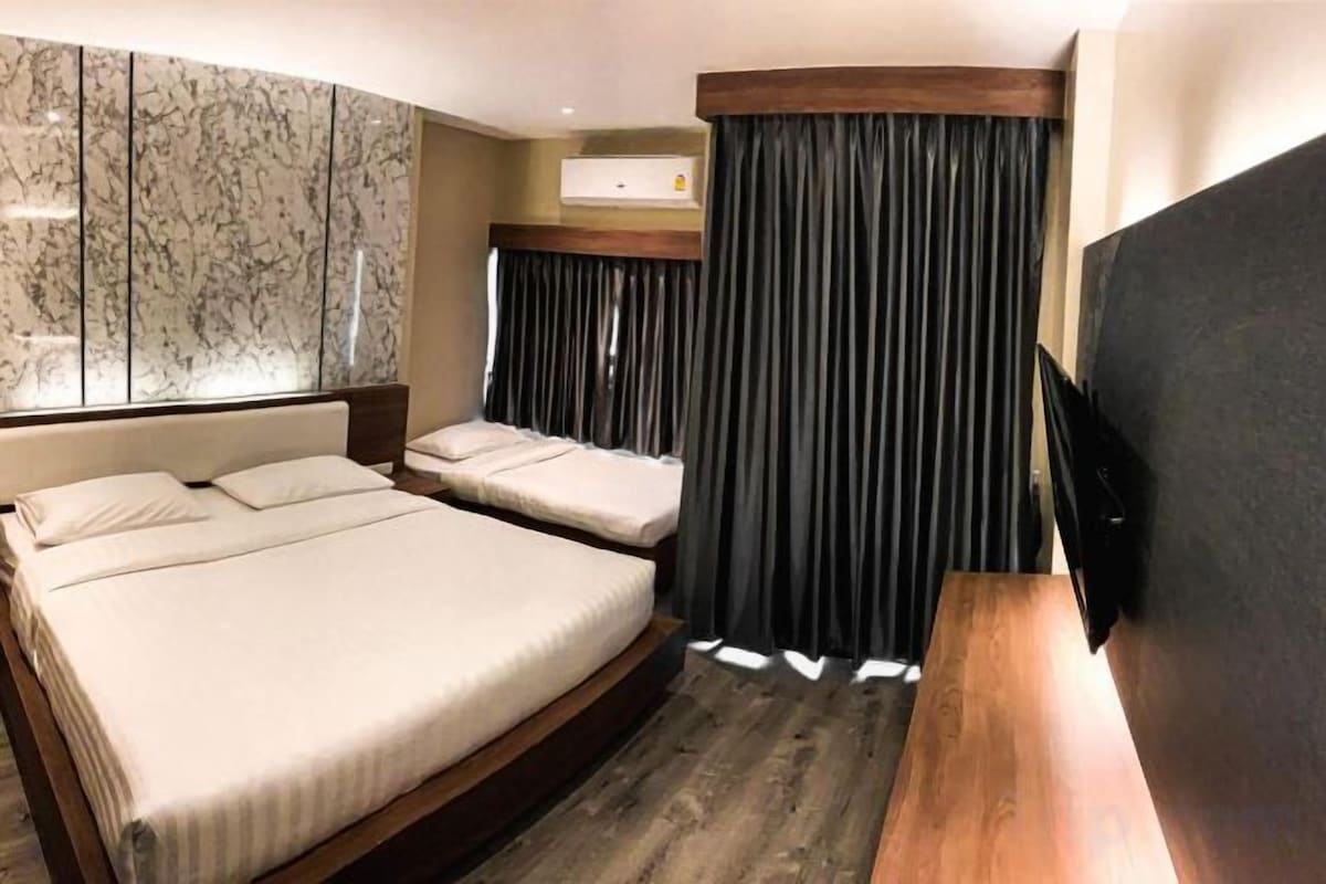 A hotel room with a large bed, a smaller bed, a flat-screen TV, and a marble wall.