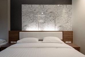 Une chambre d’hôtel moderne avec une tête de lit en marbre, un lit parfaitement fait et une table de chevet en bois.