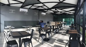 A modern dining area with tables and chairs, ceiling fans, and air conditioning units. - The Chess Hotel (Rayong)
