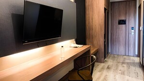 A modern hotel room with a wooden desk, a flat-screen TV mounted on the wall, a chair, and a wooden door. - The Chess Hotel (Rayong)
