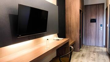 Habitación de hotel moderna con un escritorio de madera, un televisor de pantalla plana montado en la pared, una silla y una puerta de madera.