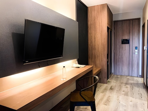 A modern hotel room with a wooden desk, a flat-screen TV mounted on the wall, a chair, and a wooden door. - The Chess Hotel (Rayong)