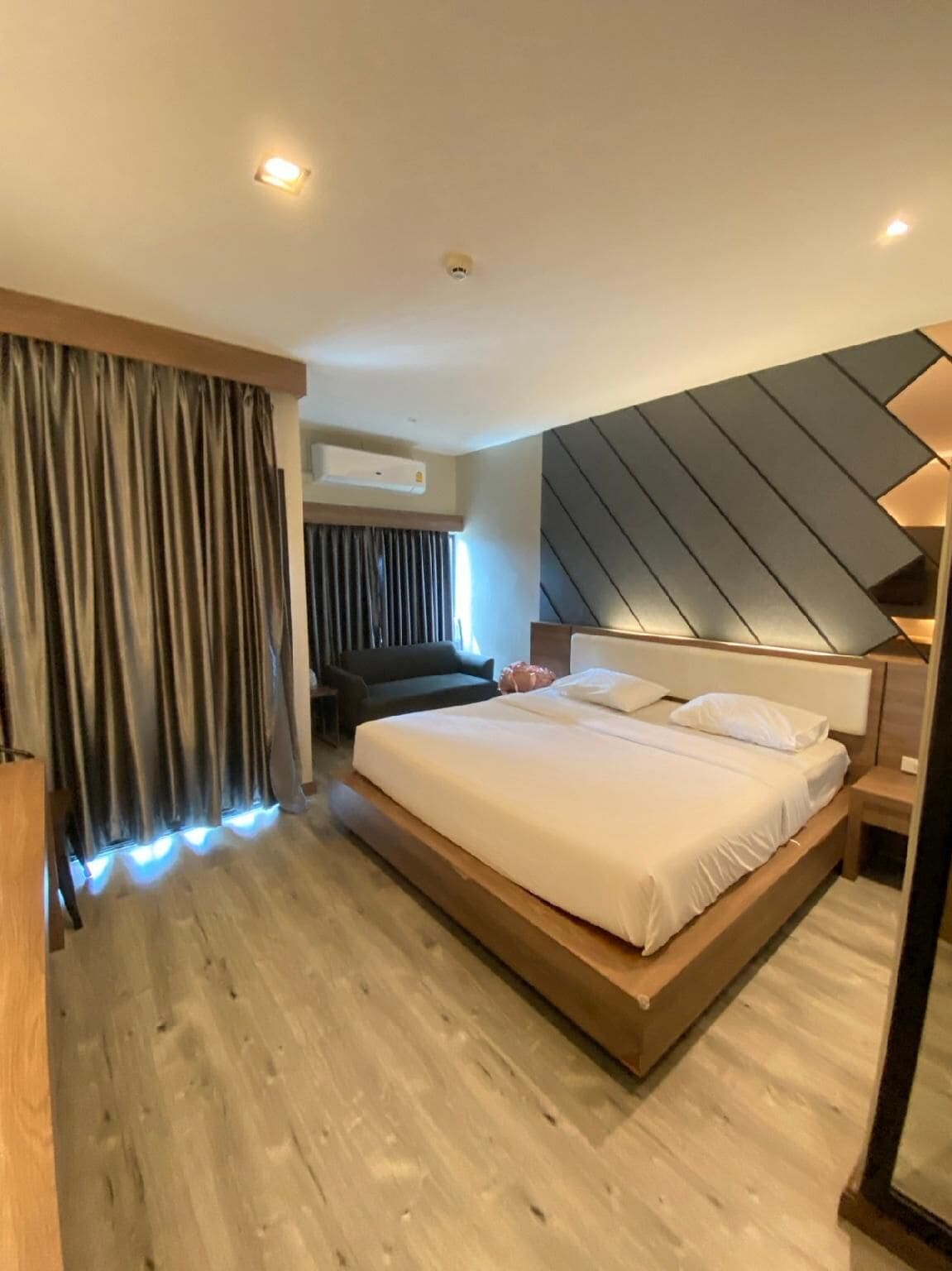 A modern hotel room with a large bed, a built-in desk, and a wall-mounted air conditioning unit.