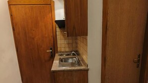 A compact kitchen with a sink, wooden cabinets, and a tiled backsplash. - Kindi Suites Hotel (Amman)