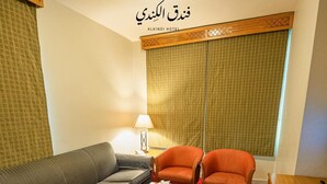 A hotel room with a sofa, two chairs, a coffee table, a lamp, and a window with patterned curtains. - Kindi Suites Hotel (Amman)