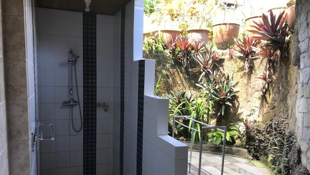 A shower area with a tiled wall and a small step leading to a balcony with potted plants. - Bali Breeze Bungalows (Ubud)