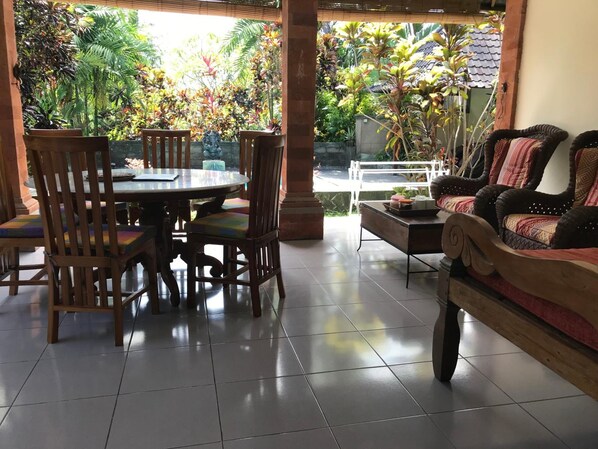 Un coin repas comprenant une table ronde et des chaises, un canapé et une vue sur un jardin où poussent différentes plantes.