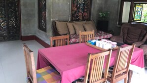 A dining area with a pink tablecloth, wooden chairs, and a sofa with cushions. - Bali Breeze Bungalows (Ubud)