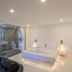 Une chambre d’hôtel moderne dotée d’un grand lit, d’une douche séparée par des parois en verre et d’un coin salon avec un fauteuil en cuir.