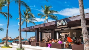 A beachside restaurant with outdoor seating, palm trees, and a clear blue sky. - Marival Emotions Resort & Suites Riviera Nayarit by Mercure (Nuevo Nayarit)