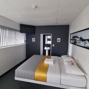 A hotel room with a bed, a window with blinds, a sink, and a framed picture on the wall. - Check Inn Hotel (Cape Town)