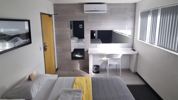 A hotel room with a bed, a desk, a chair, and a view of a bridge. - Check Inn Hotel (Cape Town)