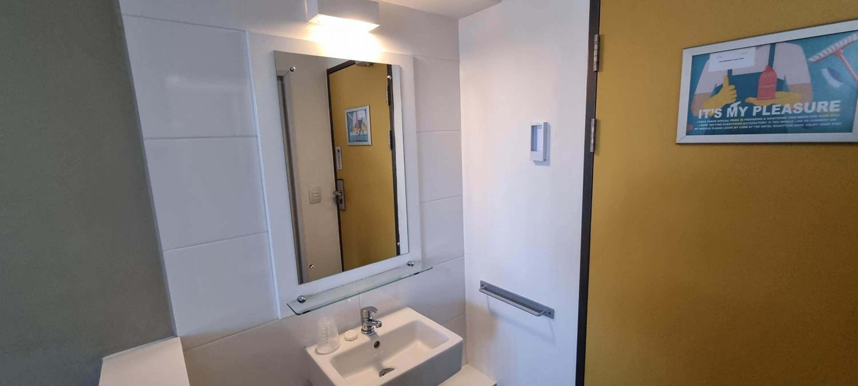 Un baño con un lavamanos blanco, un espejo y una pared amarilla.