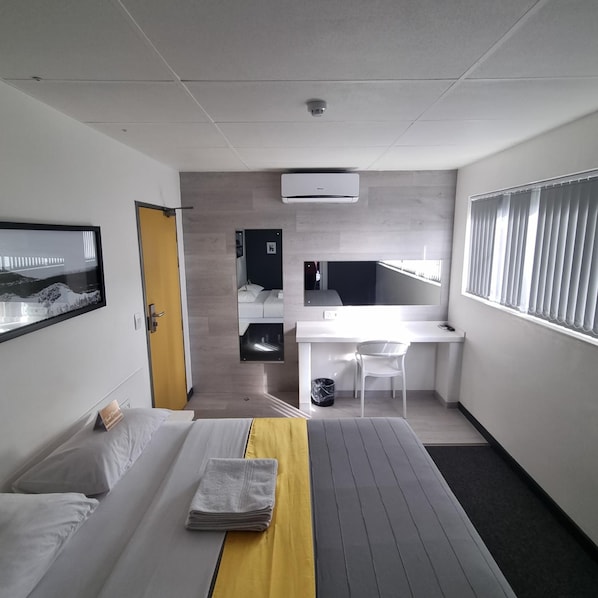 A hotel room with a bed, a desk, a chair, and a view of a bridge. - Check Inn Hotel (Cape Town)