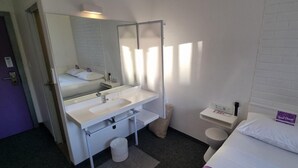 A hotel room with a bed, a white sink, a mirror, and a toilet. - Check Inn Hotel (Cape Town)