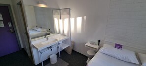 A hotel room with a bed, a white sink, a mirror, and a toilet. - Check Inn Hotel (Cape Town)