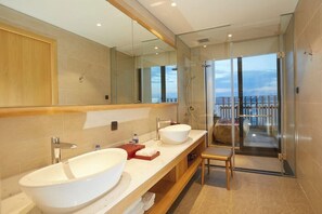 Une salle de bain moderne avec deux grands lavabos, une douche en verre et vue sur le balcon.
