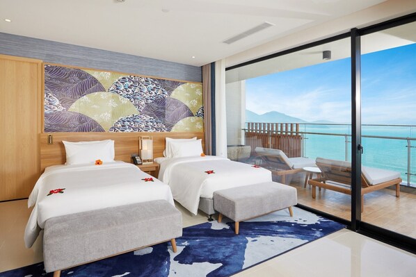 Une chambre d’hôtel avec deux lits, une grande fenêtre donnant sur la mer et un balcon avec des sièges.