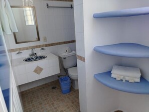 Un baño con lavamanos, inodoro y repisas.