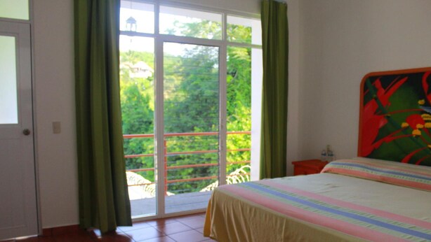A bedroom with a bed, a window with curtains, and a view of greenery outside. - Hotel Mexico Lindo (Santa María Huatulco)