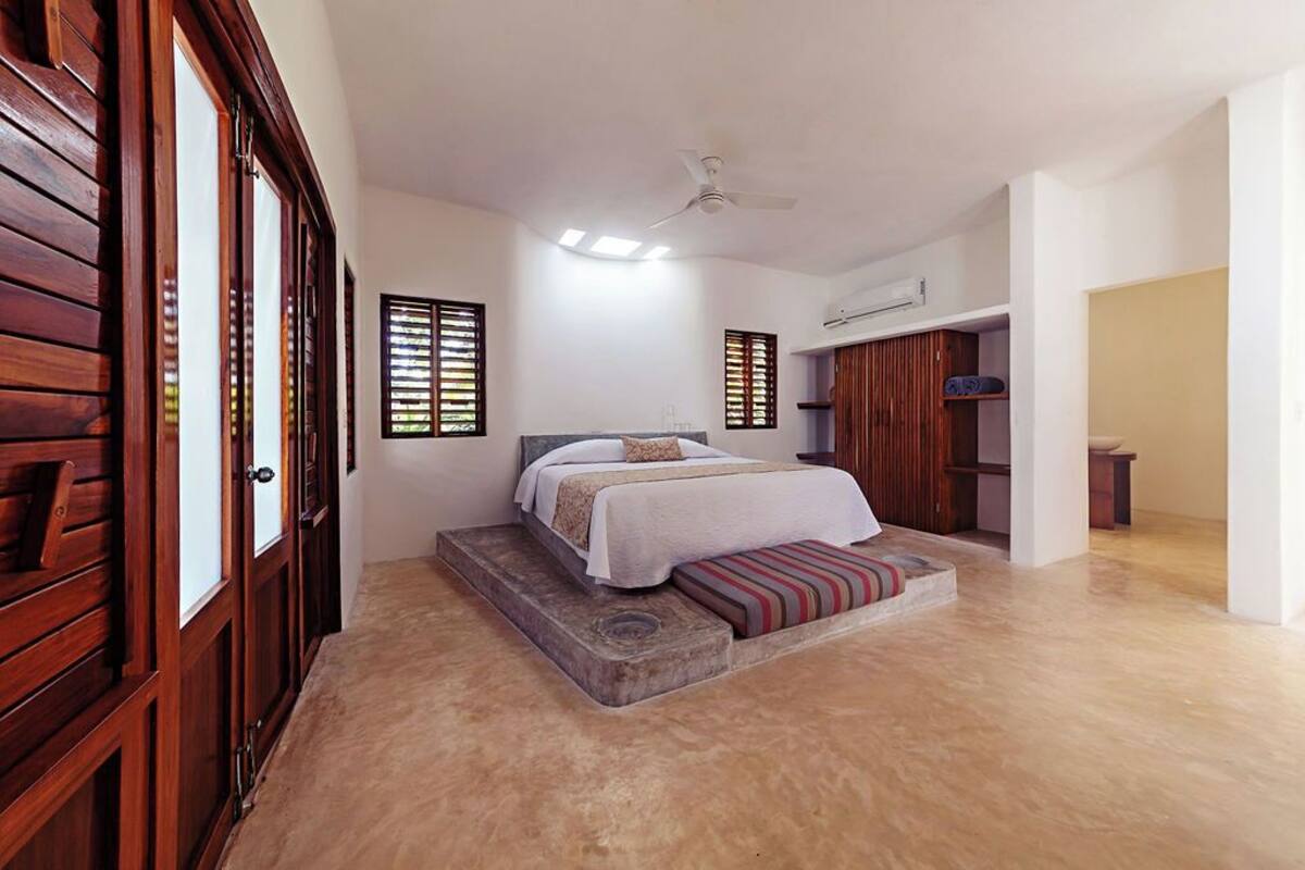 A bedroom with a bed, a wooden wardrobe, a ceiling fan, and a window with blinds.