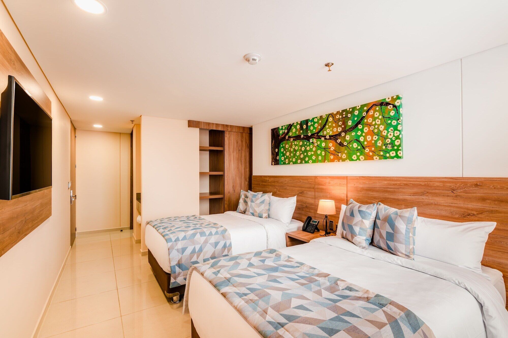 A hotel room with two beds, a TV mounted on the wall, a painting, and a wooden headboard.