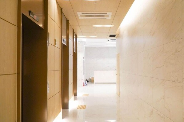 A corridor with wooden paneling on the left, a white reception desk in the distance, and a tiled floor. - J-one Hotel and Resort (Cheongju)