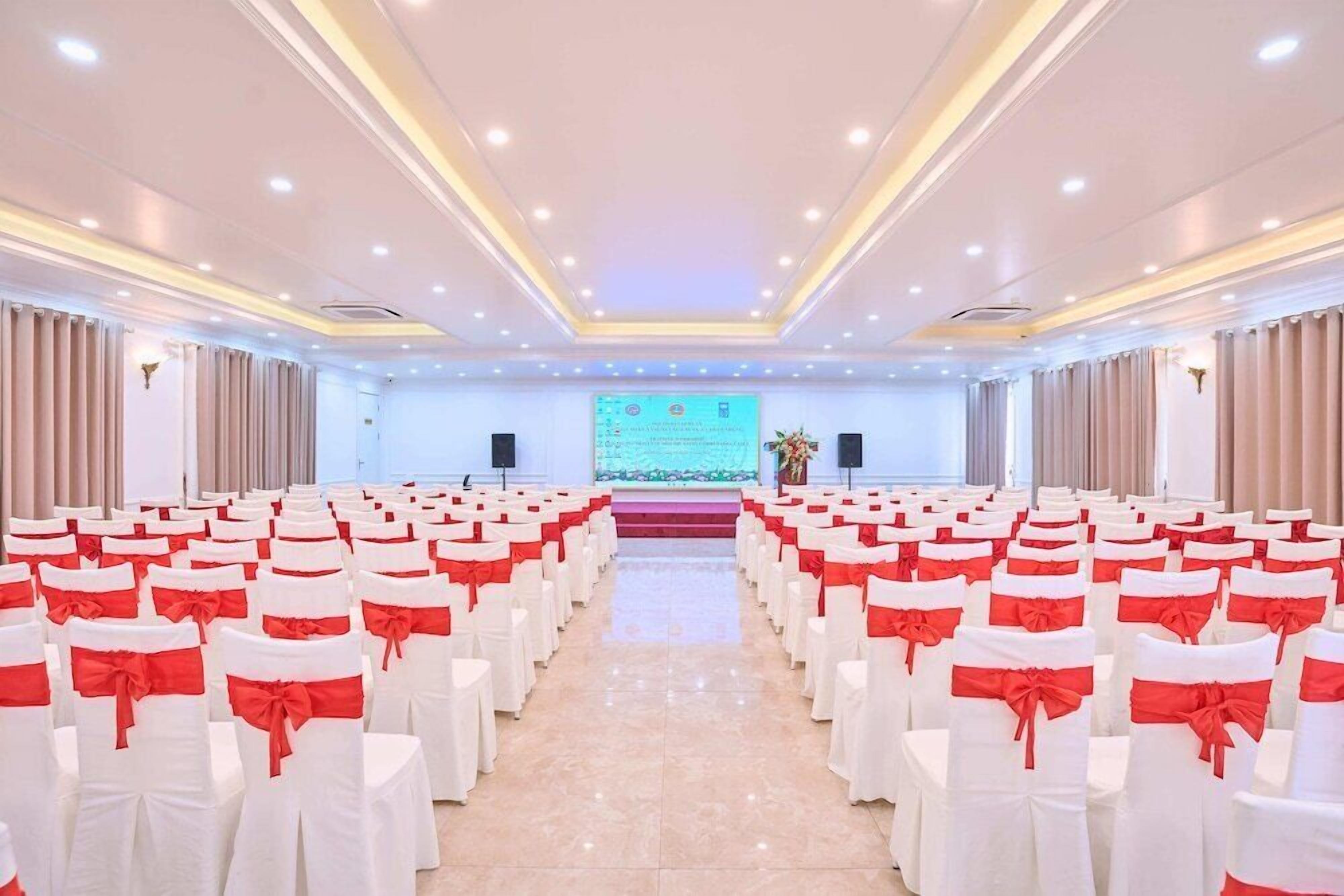A conference room with rows of white chairs with red sashes, a stage with a presentation screen, and a podium.