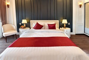 Habitación de hotel con cama, dos mesitas de noche, una silla y cabecera con paneles verticales.