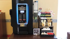 A coffee machine with a digital display, a menu board, and various coffee pods and utensils on a counter.
