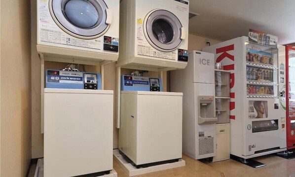 Une laverie équipée de plusieurs machines à laver et de plusieurs sèche-linge, ainsi que d’un distributeur automatique et d’un réfrigérateur.