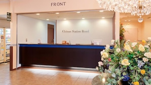 A reception desk with a sign reading "Chitose Station Hotel" and a chandelier above.