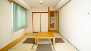 A traditional Japanese room with tatami flooring, a wooden table, sliding doors, and a window with curtains.