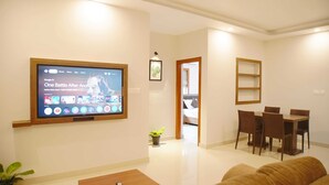 A modern living room with a flat-screen TV, a sofa, a coffee table, and a dining area with chairs and a table.