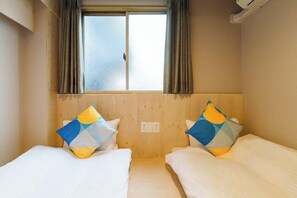 Una habitación con dos camas, cada una con almohada, una ventana con cortinas y cabecero de madera.