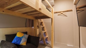 Une pièce avec un lit superposé, une échelle, un canapé avec un coussin et un climatiseur fixé au mur.