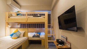Een slaapkamer met stapelbed, televisie, bureau met computer en een afvalbak.