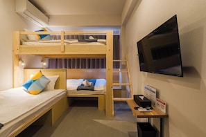 Une chambre avec un lit superposé, une télévision, un bureau avec un ordinateur et une poubelle.