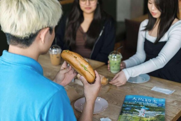 A person holding a baguette at a table with a menu and a drink. - Doyanen Hotels Bakuro (Osaka)