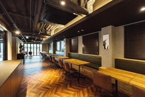 Un intérieur moderne avec un plancher en bois, de longues tables et des chaises, ainsi que de grandes fenêtres.