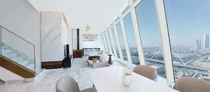 A modern hotel room with a large window offering a city view, a marble floor, and a dining area with a table and chairs. - Velero Doha (Doha)