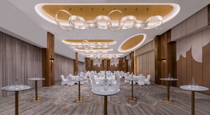 A spacious banquet hall with round tables and chairs, elegant chandeliers, and a patterned carpet. - Velero Doha (Doha)