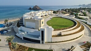 A modern hotel with a pool, a large lawn, and a view of the sea and a rocky island. - Royal M Resort Al Aqah Beach Resort (Al Aqah)