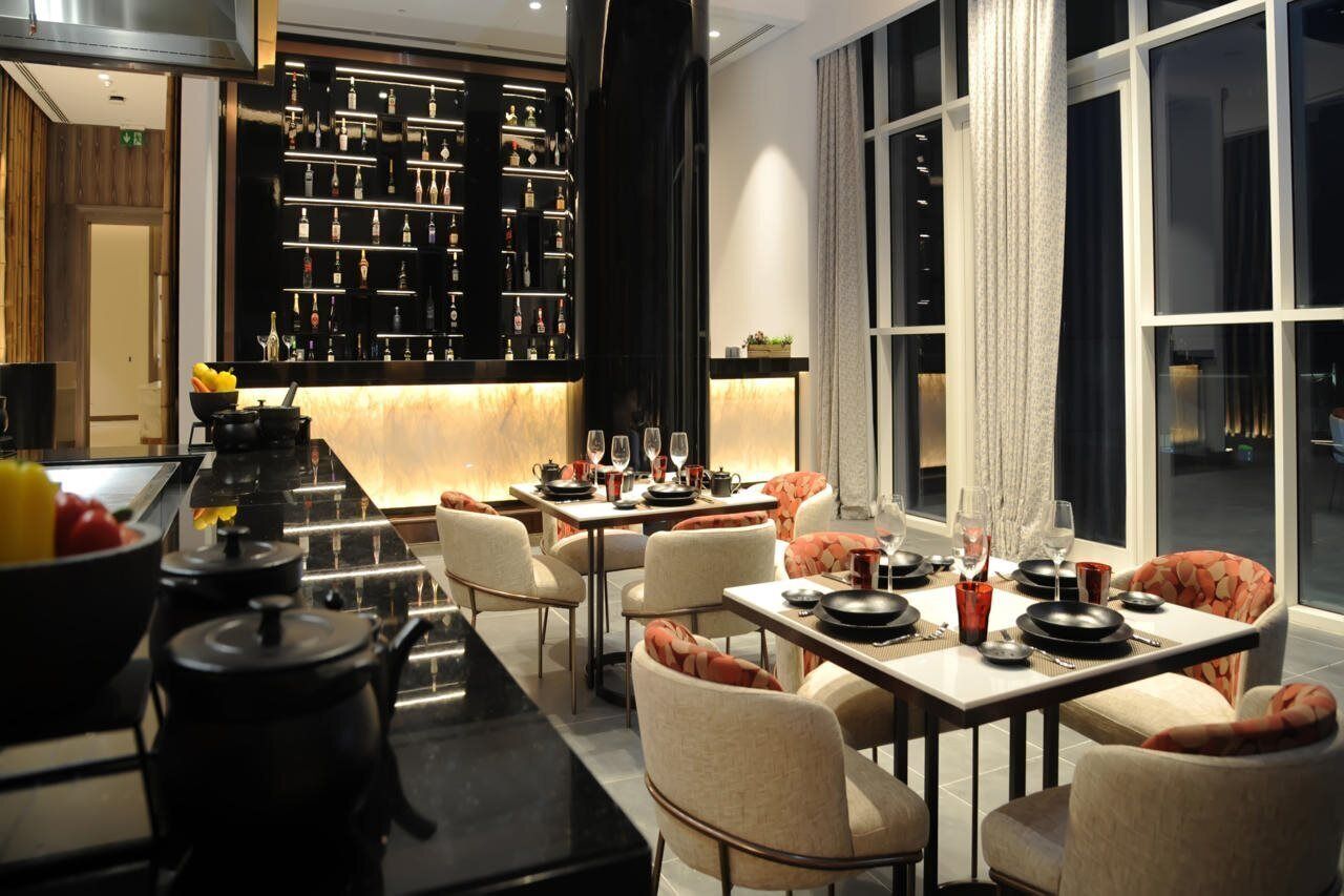 A modern dining area with a bar, a kitchen area, and a large window providing a view of the cityscape.